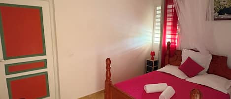 Un dormitorio con una cama de madera, una puerta verde y roja, y una pared blanca.