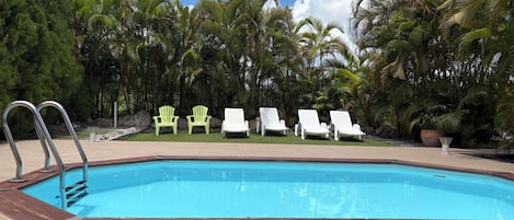 Una piscina con sillones de descanso y una escalera metálica.