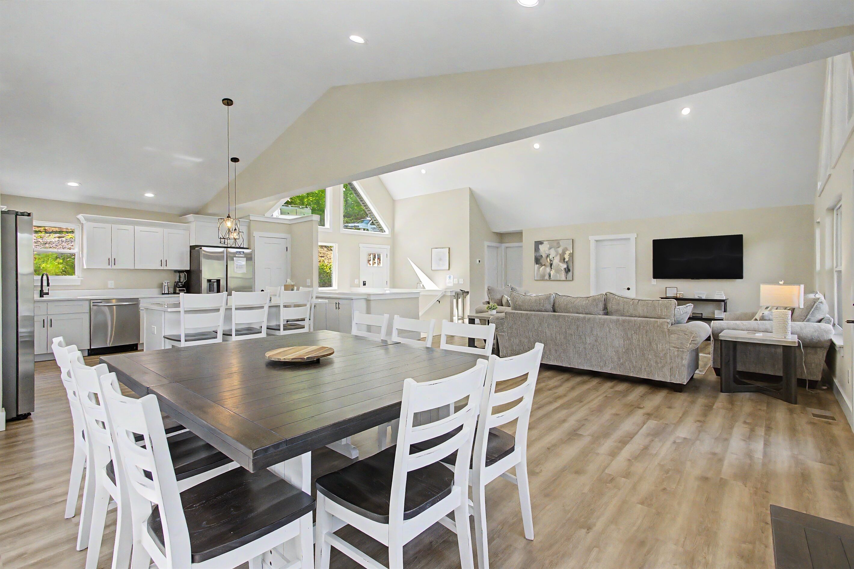A spacious living area with a dining table, white chairs, a grey sofa, and a flat-screen TV.