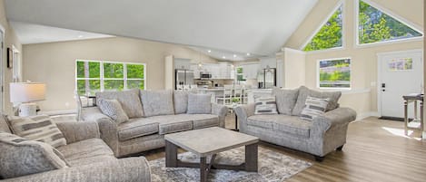 A spacious living area with a sectional sofa, a coffee table, and a dining area with a kitchen in the background.
