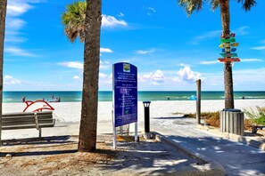 Une plage avec un panneau indicateur, des palmiers et un banc.