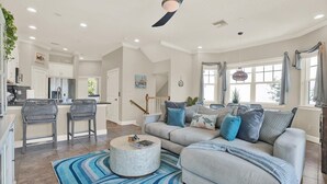A spacious living room with a grey sofa, blue and white striped rug, and a ceiling fan.