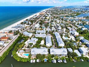 Vue aérienne d’une zone résidentielle côtière, avec une plage, un port de plaisance et un grand hôtel composé de plusieurs bâtiments.