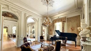 Une vaste pièce agrémentée d’un magnifique piano à queue, de fauteuils richement décorés et d’un lustre.