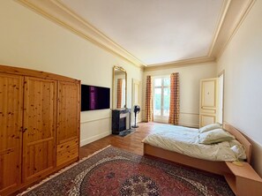 A bedroom with a bed, wooden wardrobe, a flat-screen TV, a fireplace, and a large window with curtains. - 19th-Century Chateau in Loire Valley with 106 acres of stunning grounds (Hommes)