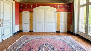 Une pièce dotée d’un grand tapis décoratif, de trois portes blanches et d’un mur rouge orné de motifs dorés.