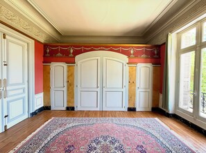 A room with a large, ornate rug, three white doors, and a red wall with gold trim. - 19th-Century Chateau in Loire Valley with 106 acres of stunning grounds (Hommes)