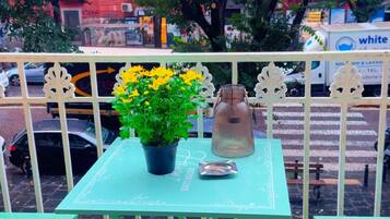 A green outdoor seating area with a table and chairs, a potted plant with yellow flowers, and a decorative vase.