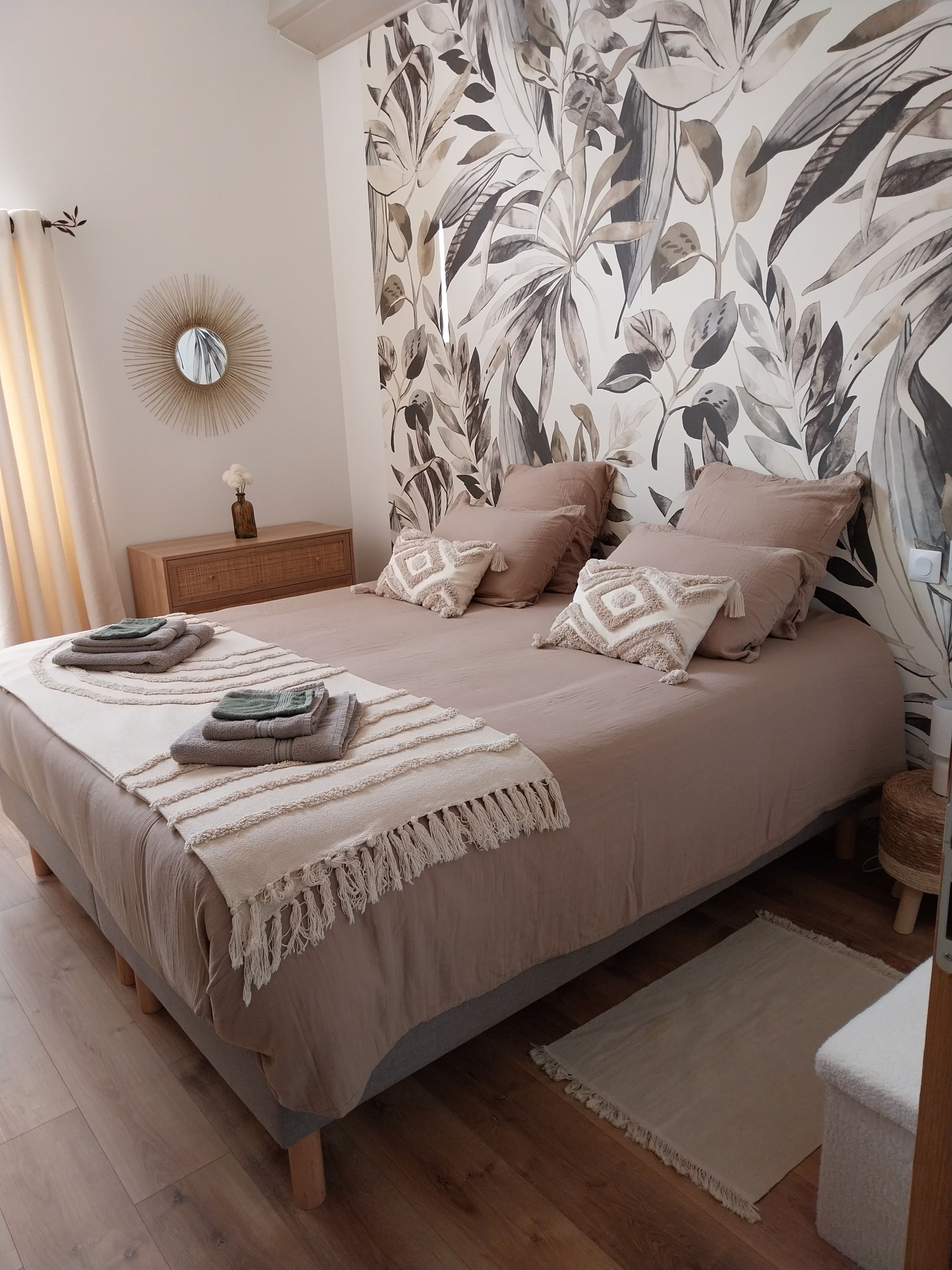 Une chambre avec un grand lit, un miroir rond et un mur orné d’un motif de feuilles.