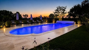 A swimming pool with a curved edge, surrounded by lounge chairs and umbrellas, and a grassy area with flowers.