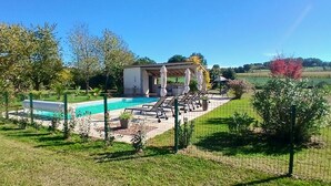 A swimming pool with lounge chairs, a pergola with umbrellas, and a fenced garden area.