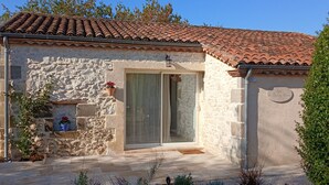 A stone building with a tiled roof, a glass door, and a small porch area with potted plants.