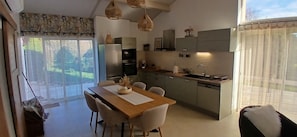 A modern kitchen with a dining area, large windows, and a view of the outdoors.