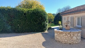 A house with a stone circular patio, a garden with a large hedge, and a tiled roof.