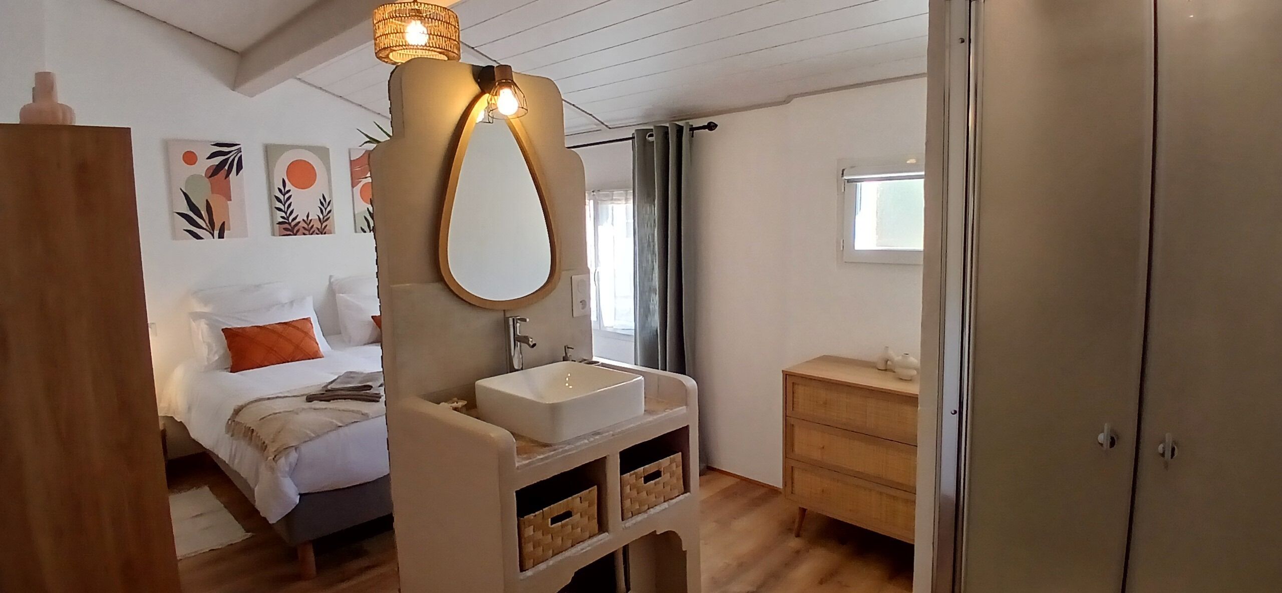 A bedroom with a bed, a bedside table, a mirror, a sink, and a wardrobe.