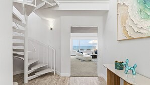 Un interior moderno con una escalera blanca, vistas al océano a través de grandes ventanales y una decoración minimalista.