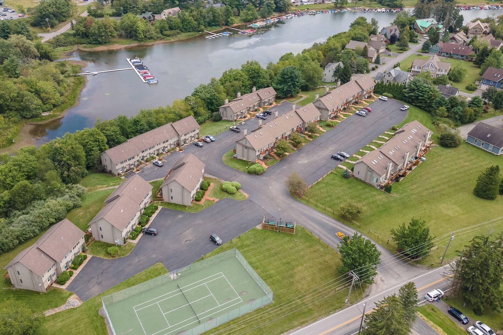 An aerial view of a residential area with houses, a tennis court, and a body of water.