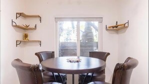 A dining area with a round table, four chairs, and three wall-mounted shelves with decorative items. - Charming Pied-e-terre near the beach for a relaxing getaway (Los Angeles)