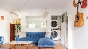A living room with a blue sofa, a coffee table, a guitar, and a washing machine. - Charming Pied-e-terre near the beach for a relaxing getaway (Los Angeles)
