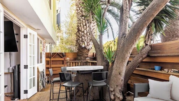 An outdoor seating area with a round table and chairs, a wooden bench, a white sofa, and a large tree. - Charming Pied-e-terre near the beach for a relaxing getaway (Los Angeles)