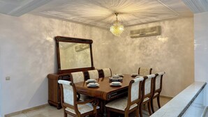 Comedor con una gran mesa de madera, seis sillas, una araña y un espejo grande en la pared.