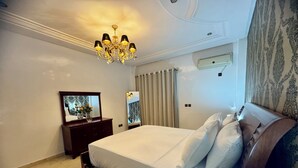 Habitación de hotel con una cama grande, una mesita de noche de madera, un espejo, una araña y un equipo de aire acondicionado, además de una cortina estampada.