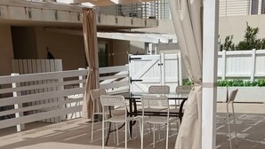 Un espacio de estar al aire libre con una pérgola, sillas blancas y una mesa.