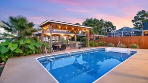 A swimming pool with a wooden deck, a covered patio area, and surrounding greenery. - Canal front, Heated pool, Boat lift, Pet friendly (Gulf Breeze)