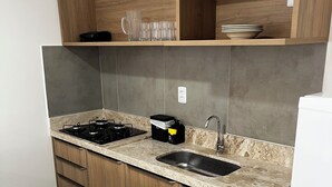 Una cocina compacta con estufa a gas, un fregadero, muebles de madera y encimera de mármol.