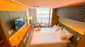 A hotel room with a bed, a TV, a desk, and a dining area.