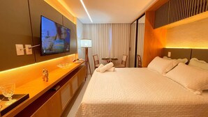 A hotel room with a large bed, a television mounted on the wall, a desk with a lamp, and a small table with chairs. - Setai Aquamaris Vista Mar Lateral (João Pessoa)