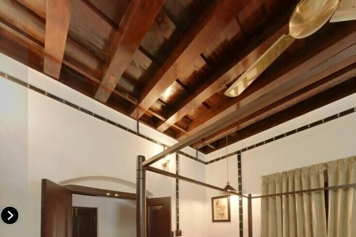Una cama con dosel y tablero de madera, suelo con estampado verde y blanco, y techo con vigas de madera a la vista.
