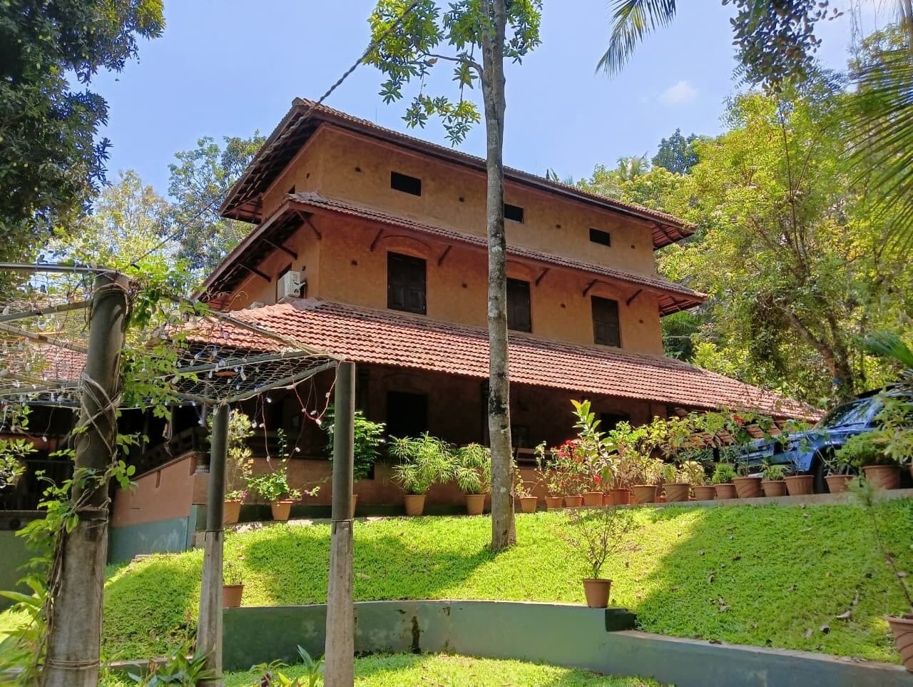 A two-story building with a red-tiled roof, surrounded by greenery and potted plants.