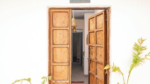 Une porte en bois, sur laquelle est accrochée une enseigne, donne accès à une pièce dotée d’un ventilateur de plafond et d’un tapis à motifs.