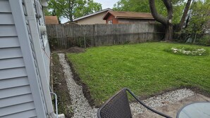 Un patio trasero con valla de madera, césped y una zona de patio con una silla y una mesa.