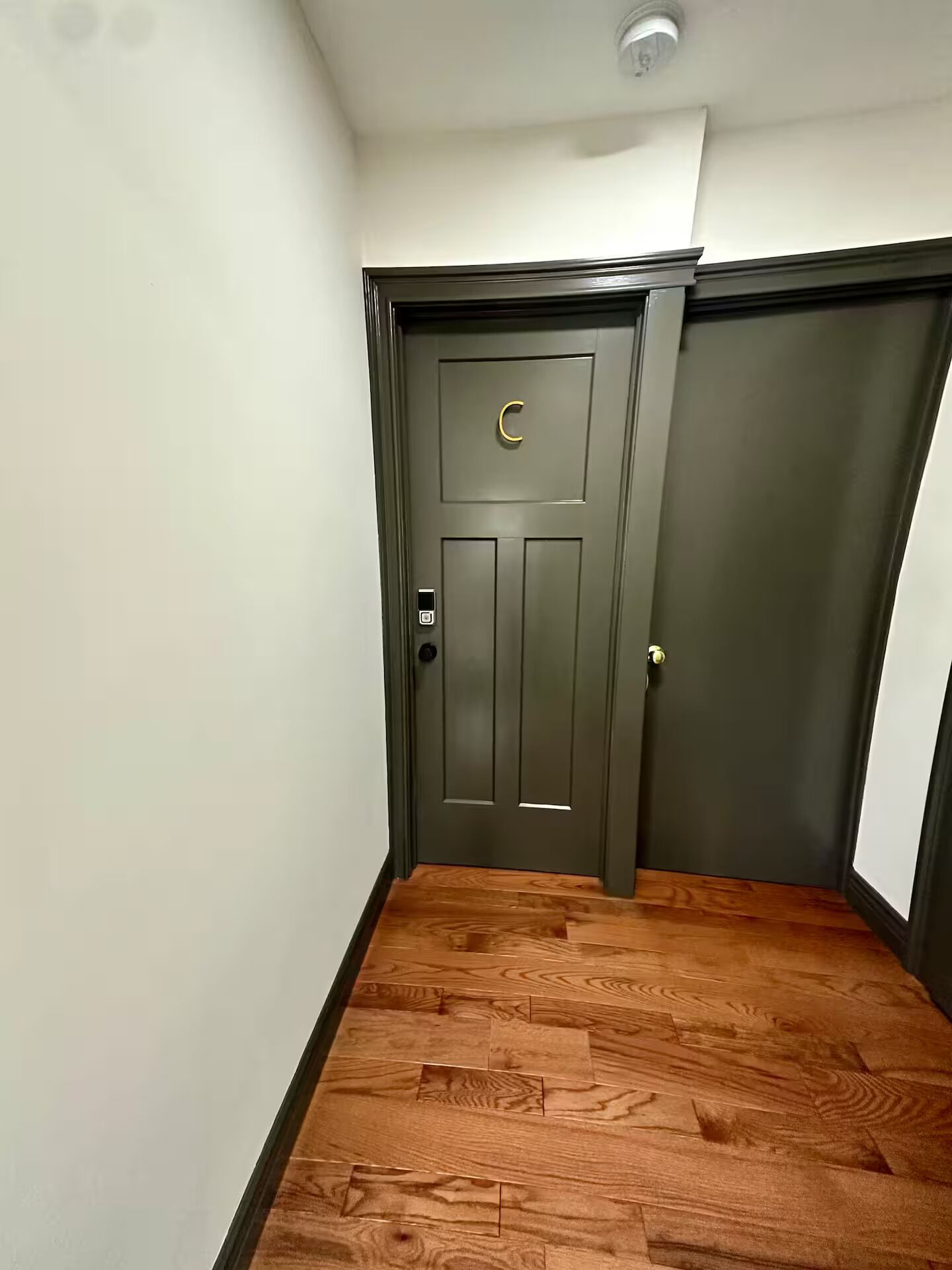 Un pasillo con piso de madera y una puerta gris oscuro con picaporte dorado y teclado electrónico.
