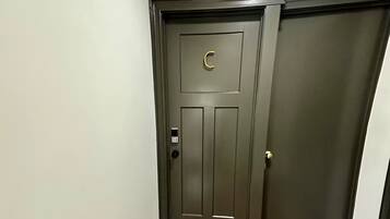 Un pasillo con piso de madera y una puerta gris oscuro con picaporte dorado y teclado electrónico.