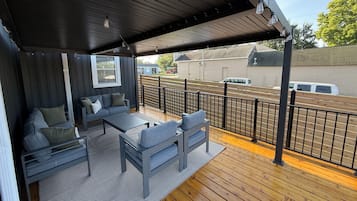 Uma área de estar coberta ao ar livre com um deck de madeira, um sofá e uma mesa.