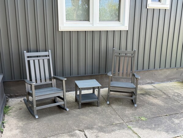Two wooden chairs and a small table outside a building with vertical siding.