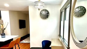 A modern room with a wooden floor, a desk with a chair, a chandelier, and two wall clocks.