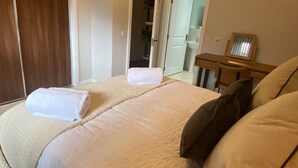 A bedroom with a bed, a wooden nightstand, a mirror, and a door leading to a bathroom. - TravelNess Apartment (Inverness)