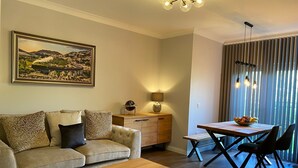 A living room with a sofa, coffee table, dining table with chairs, a lamp, and a painting on the wall. - TravelNess Apartment (Inverness)