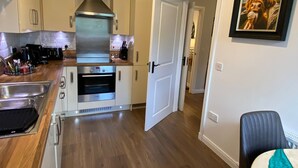 A modern kitchen with stainless steel appliances, wooden flooring, and a door leading to another room. - TravelNess Apartment (Inverness)