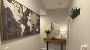 A hallway with a world map, a wooden console table with a vase of flowers, a round mirror, and a telephone. - TravelNess Apartment (Inverness)