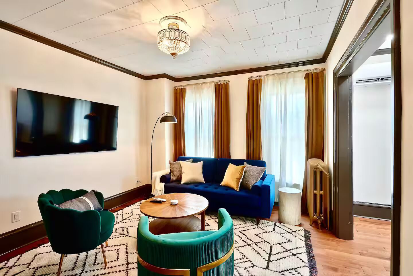 Un salon moderne avec un canapé bleu, des fauteuils verts, une table basse ronde et un téléviseur à écran plat fixé au mur.