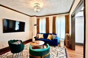 A modern living room with a blue sofa, green armchairs, a round coffee table, and a flat-screen TV mounted on the wall.