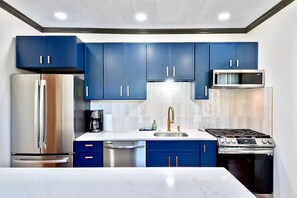 A modern kitchen with blue cabinets, stainless steel appliances, and a white marble countertop.