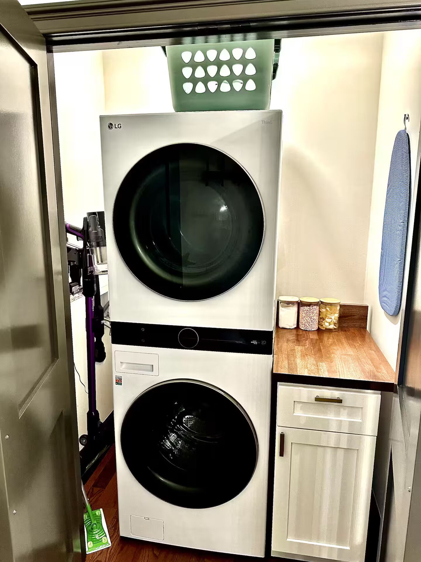 Un appareil compact combinant lave-linge et sèche-linge, doté d’un panneau de commande, d’un petit meuble et d’une serviette accrochée au mur.