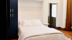 A bedroom with a bed, a wardrobe, a nightstand, and a door leading to another room.