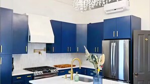 A modern kitchen with blue cabinets, a stainless steel refrigerator, a gas stove, and a white countertop.